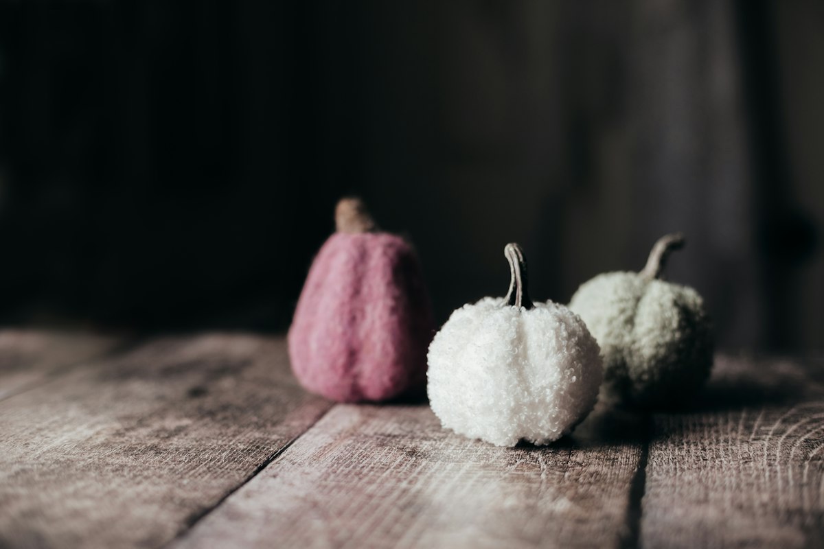Three fuzzy pumpkins, mauve, white and pale green, on old weathered wood