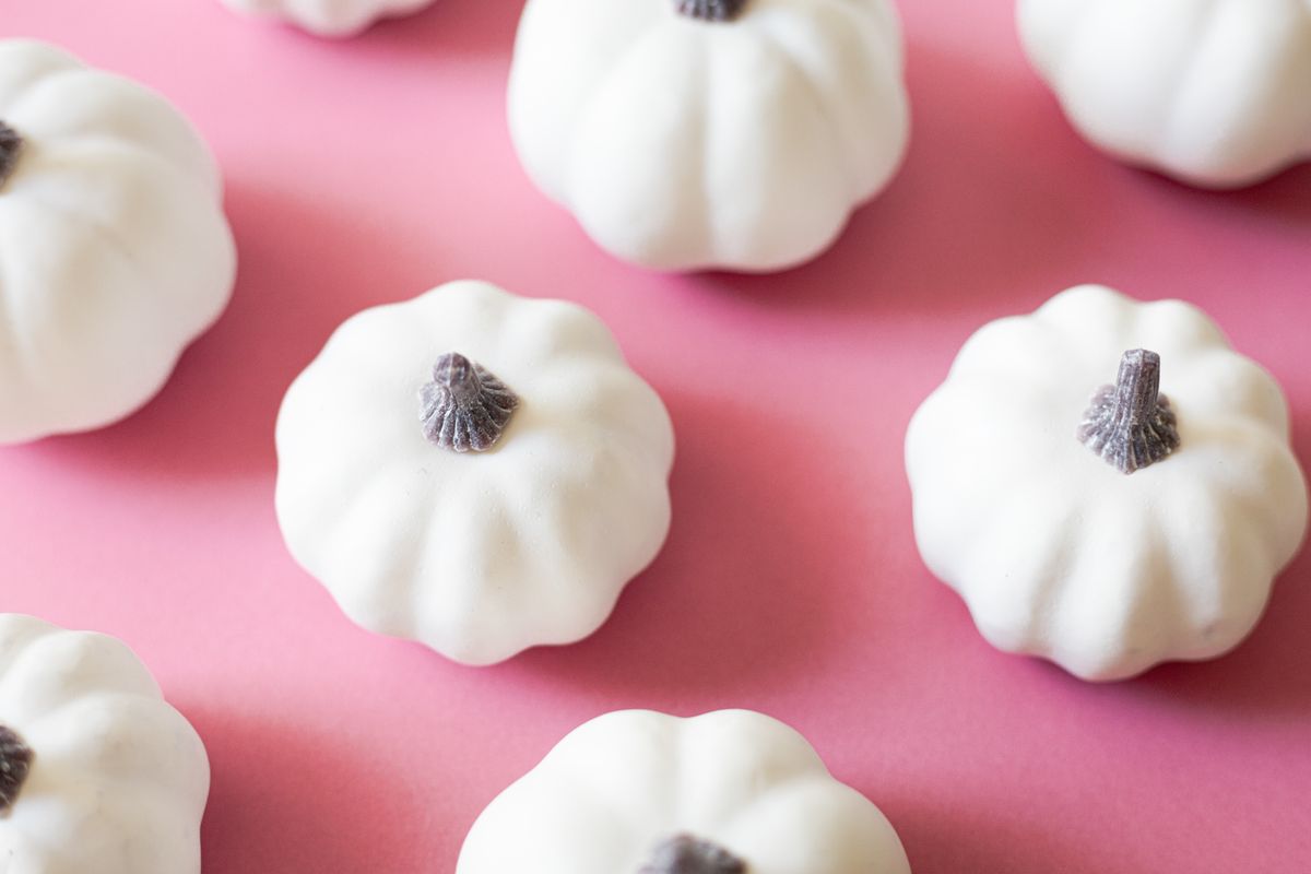 Little white pumpkins scattered on a bright pink surface