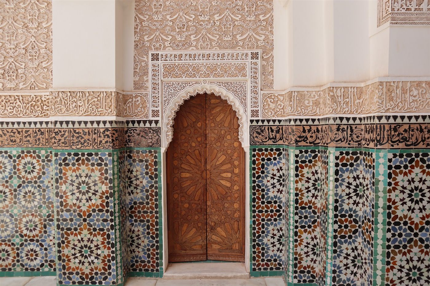 Zellige tile in star patterns and carved plaster framing a wooden door in Morocco