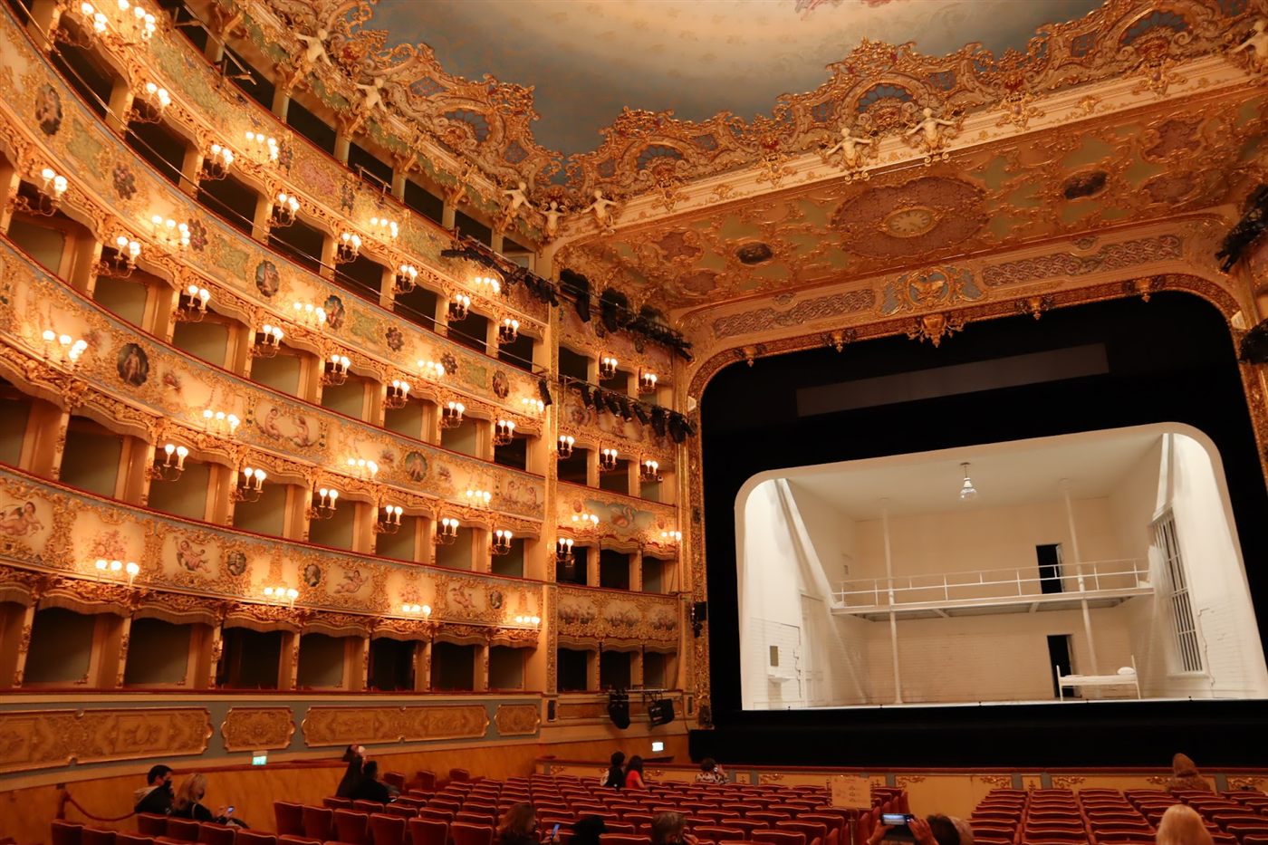 Gilded tiers of opera boxes glowing around the stage of an opera house in Venice