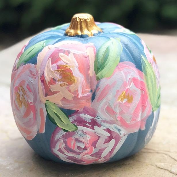 A pumpkin painted matte blue with big loose pink and coral peonies, green leaves and a gold stem