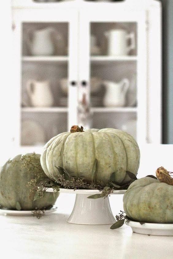 Sage green pumpkins on white cake stands with dried seeded eucalyptus