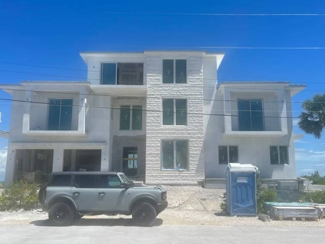 The house under construction: three stories in white stucco with the ledgestone spine up the center, windows in, scaffolding gone